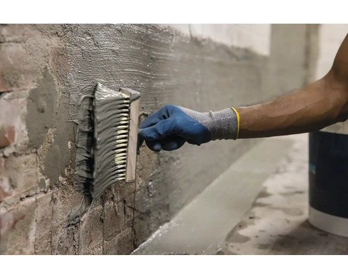 Osoba nanáší štětcem hydroizolační stěrku na stěnu.