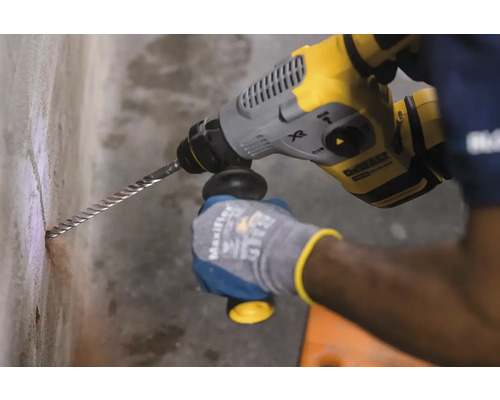 Osoba vrtá otvory do zdi pomocí vrtacího kladiva.