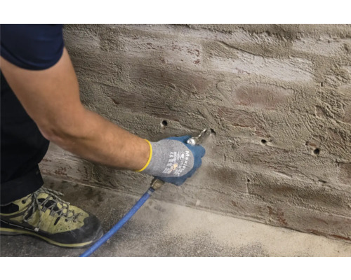 Muž čistí otvory pro vrtání v cihlové zdi stlačeným vzduchem.