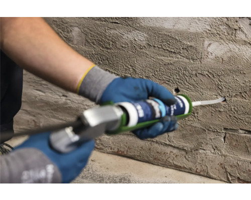 Řemeslník vyplňuje otvor ve zdi tmelem z kartuše.