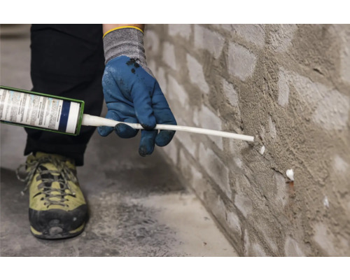 Osoba utěsňuje cihlovou zeď tmelem