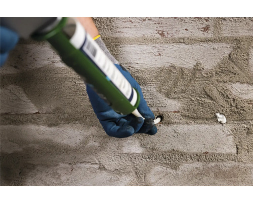 Osoba plní otvor v cihlové zdi pomocí kartuše.