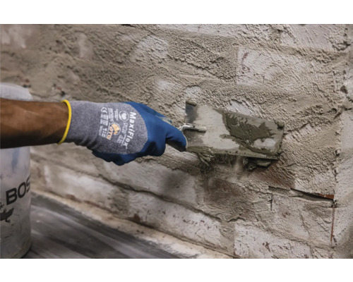 Osoba nanáší maltu na cihlovou zeď pomocí lžíce.