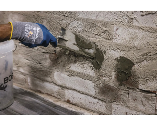 Osoba nanáší spárovací hmotu na cihlovou zeď pomocí lžíce
