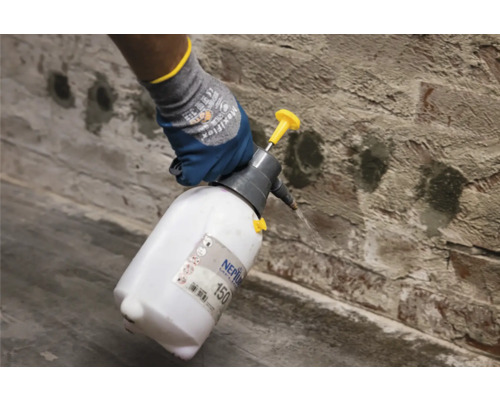 Osoba používá tlakový postřikovač značky Neptun na cihlovou zeď