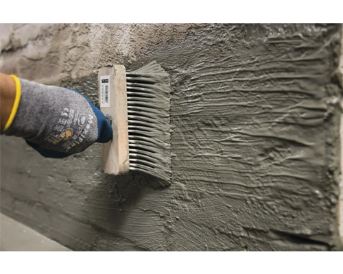 Řemeslník nanáší omítku na stěnu pomocí zubové stěrky