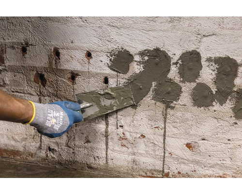 Osoba vyplňuje špachtlí otvory v cihlové zdi.