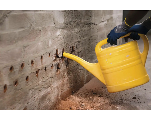 Osoba kropí cihlovou zeď žlutou konev, aby se vázal prach.