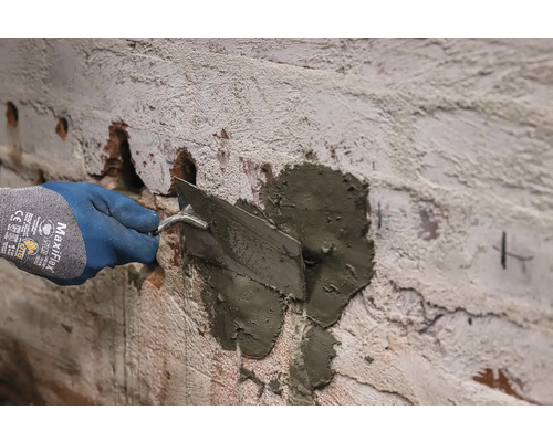 Ruka v rukavici nanáší maltu na stěnu pomocí lžíce.