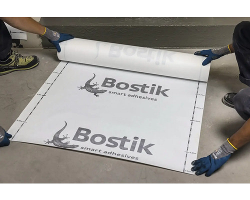 Logo Bostik. Pracovník rozvíjí těsnicí pás s měřicí stupnicí.