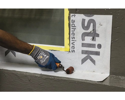 Osoba připevňuje těsnicí fólii na okno pomocí válečku.