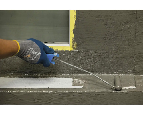 Osoba nanáší hydroizolaci na povrch pomocí malířského válečku.