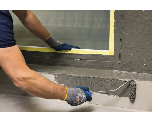 Osoba nanáší tmel pomocí malířského válečku na povrch.