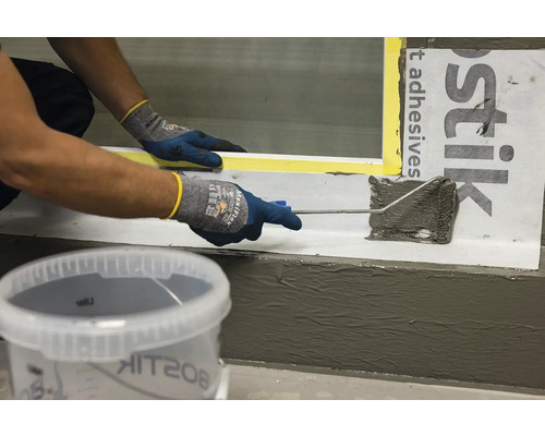 Osoba nanáší těsnicí hmotu válečkem na povrch, s kbelíkem těsnicí hmoty v popředí.