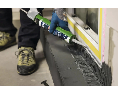 Řemeslník nanáší lepidlo na okno pomocí kartuše