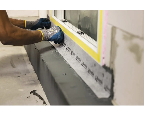 Pracovník instaluje těsnicí pásku na okenní rám.