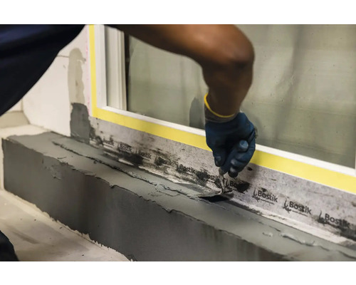 Řemeslník opracovává okenní přípojku špachtlí a těsnicí páskou