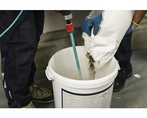 Osoba sype materiál ze sáčku do kbelíku, uvnitř je míchadlo.