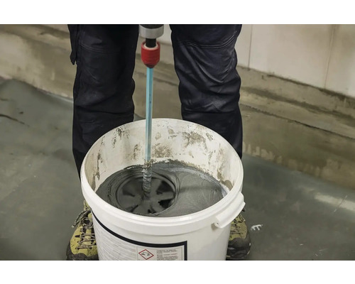 Řemeslník míchá lepidlo na dlaždice elektrickým míchadlem v kbelíku.