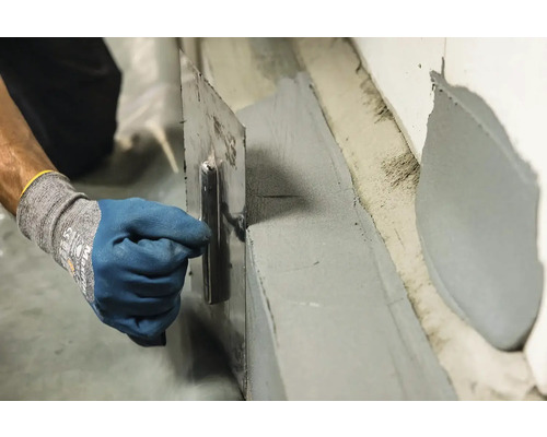 Řemeslník nanáší hydroizolační stěrku na stěnu pomocí hladítka.