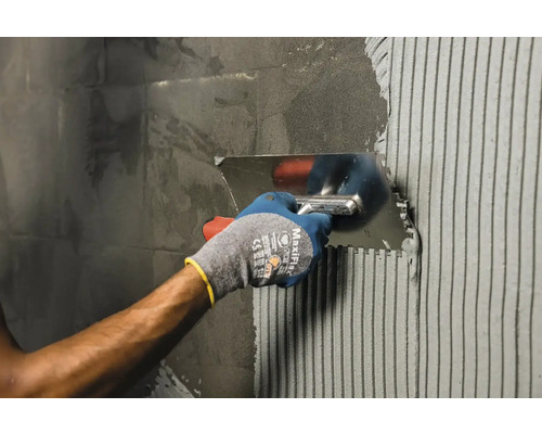 Nanášení lepidla na obklady nerezovou ocelovou lžící na zeď.