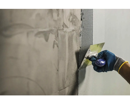 Obkladač nanáší lepidlo na stěnu pomocí špachtle