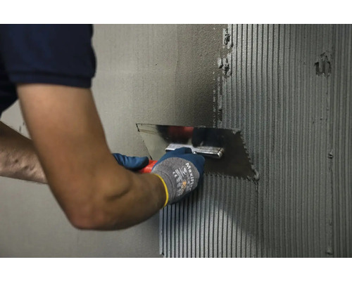 Osoba nanáší lepidlo na obklady na stěnu pomocí zubové stěrky