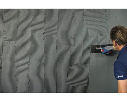 Muž nanáší lepidlo na stěnu pro pokládku obkladů.