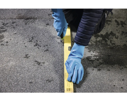 Osoba řeže nožem podél vodováhy na povrchu střechy.