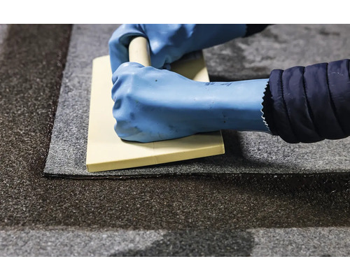 Osoba v rukavicích uhlazuje střešní pás stěrkou.