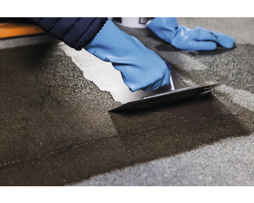 Osoba v rukavicích nanáší stěrku pomocí hladítka.