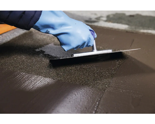 Řemeslník vyhlazuje nivelační hmotu stěrkou