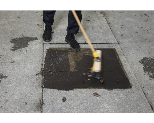 Osoba zametá tmavou tekutinu na dlažbě koštětem.