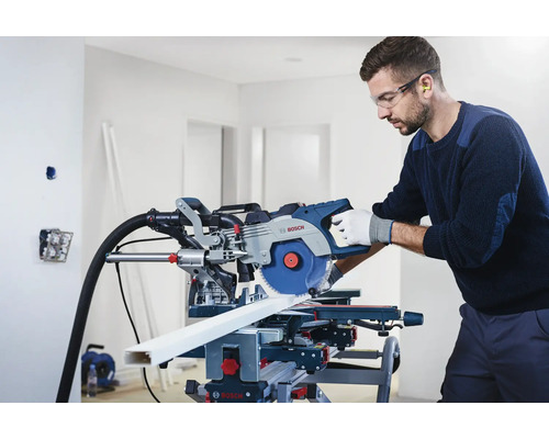 Muž s ochrannými brýlemi a chrániči sluchu používá pokosovou pilu Bosch k řezání obrobku