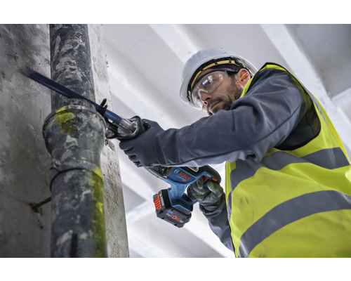 Muž řeže trubku akumulátorovou šavlovou pilou.