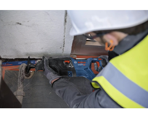 Muž s ochrannou přilbou řeže trubku pilou šavlí Bosch.