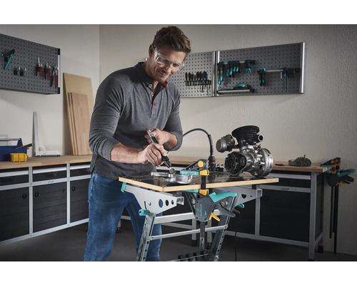 Muž pracuje s nástrojem na motoru na pracovním stole v dílně.