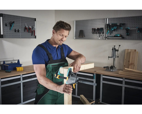 Muž pracuje s jednou rukou na kusu dřeva v dílně.