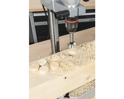 Stojanová vrtačka vrtá otvor do dřevěné desky s dřevěnými štěpkami a dřevěnými disky