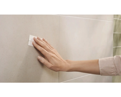 Ženská ruka přitlačuje lepicí proužek na dlaždici