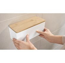 Osoba montuje bílý nástěnný box s bambusovým víkem na zeď