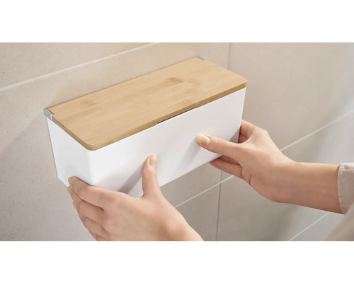 Osoba montuje bílý nástěnný box s bambusovým víkem na zeď