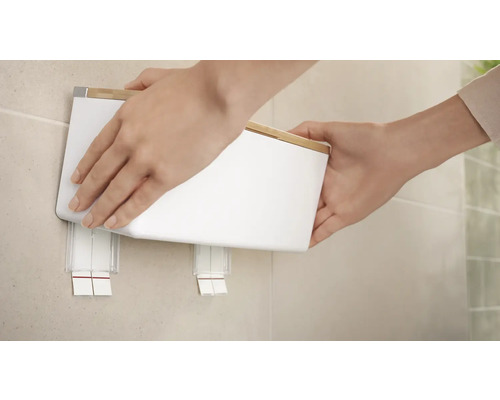 Osoba připevňuje bílou nástěnnou kosmetickou nádobu s bambusovým víkem na zeď