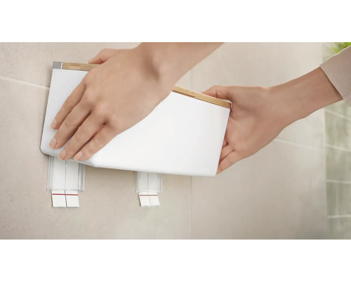 Osoba upevňuje dávkovač mýdla na zeď v koupelně