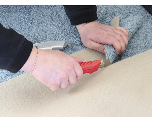 Dvě ruce řežou koberec kobercovým nožem.