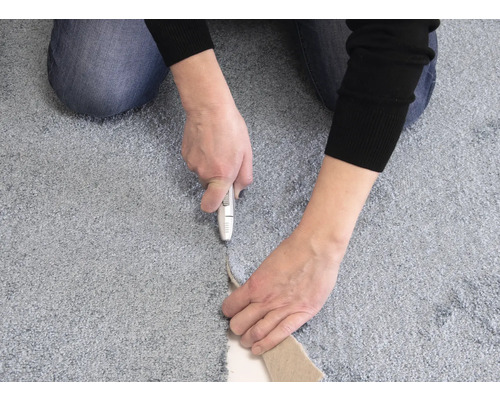 Osoba řeže koberec pomocí kobercového nože.