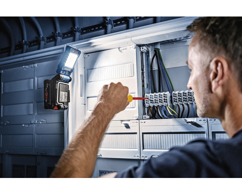 Elektrikář pracuje na rozvodné skříni s pracovním světlem Bosch.