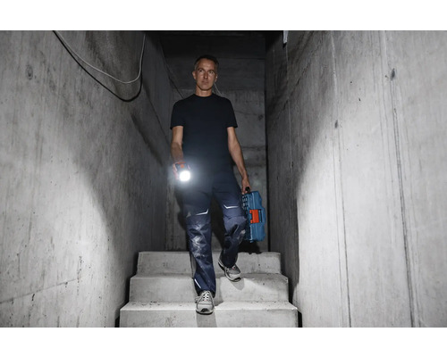 Muž schází po betonových schodech s baterkou a kufříkem na nářadí