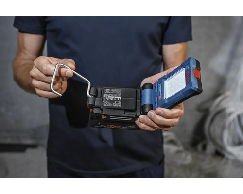 Muž drží akumulátorové pracovní světlo s hákem značky Bosch.