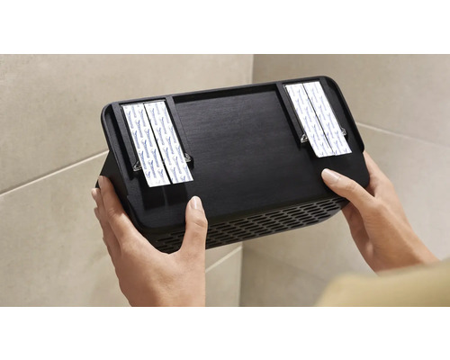 Osoba připevňuje černý nástěnný ventilátor pomocí lepicích proužků na zeď